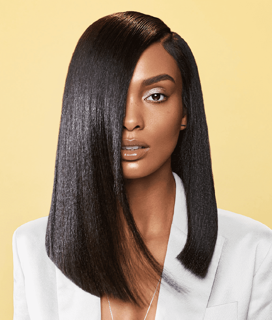 Model with sleek, straight hair and stylish outfit on a yellow background.