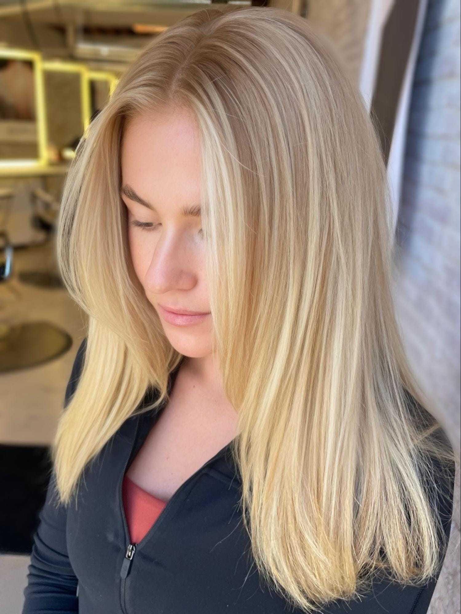 Blonde woman with straight, long hair wearing a black jacket in a salon setting.