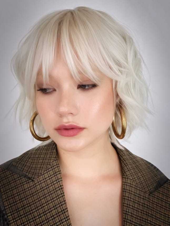 Short-haired person wearing gold hoop earrings and a plaid jacket.