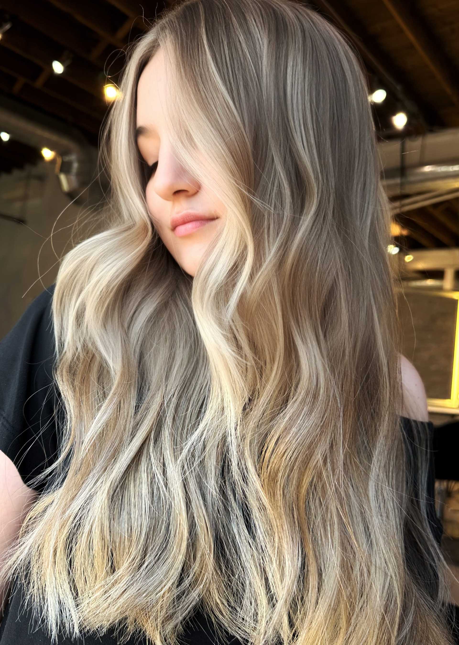 Long, wavy ash-blonde hair shines under warm lighting.